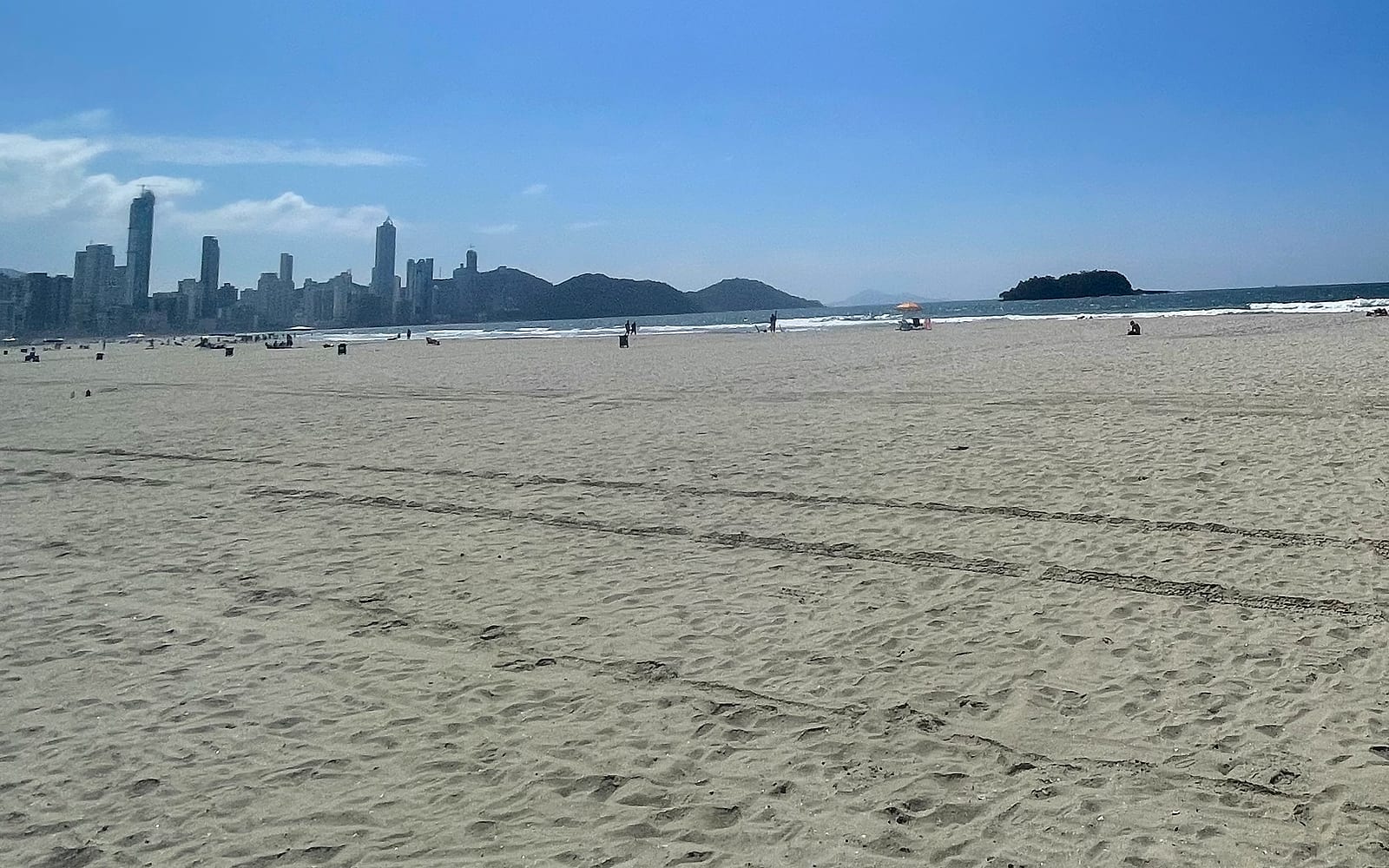 Faixa de areia larga da Praia Central de Balneário Camboriú, com o skyline da cidade ao fundo em dia de sol