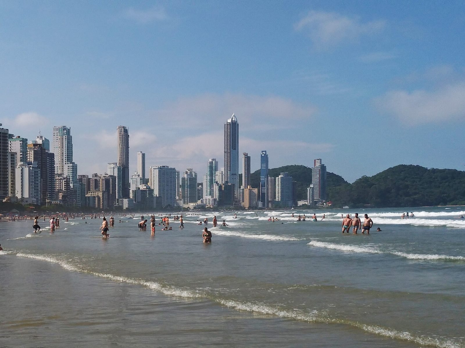 Praia central de Balneário Camboriú em dia de sol, banhistas na água e o skyline ao fundo