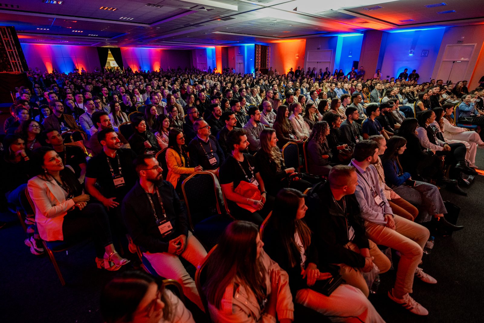 Plateia lotada acompanhando uma palestra em auditório de centro de convenções, luzes coloridas ao fundo