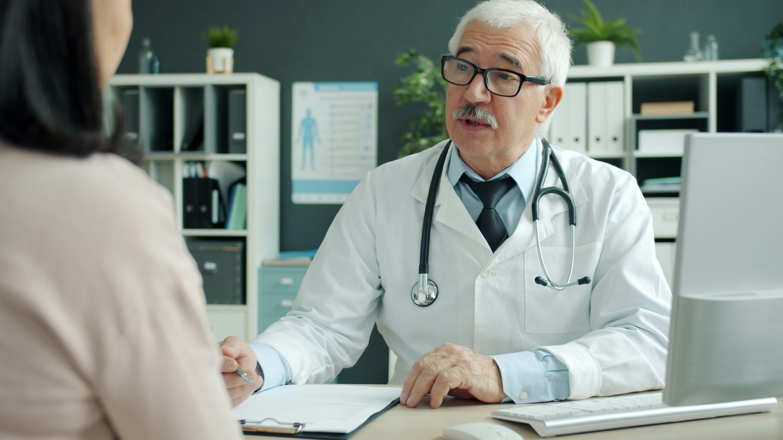 Médico conversa com uma paciente em consultório, atendendo com atenção