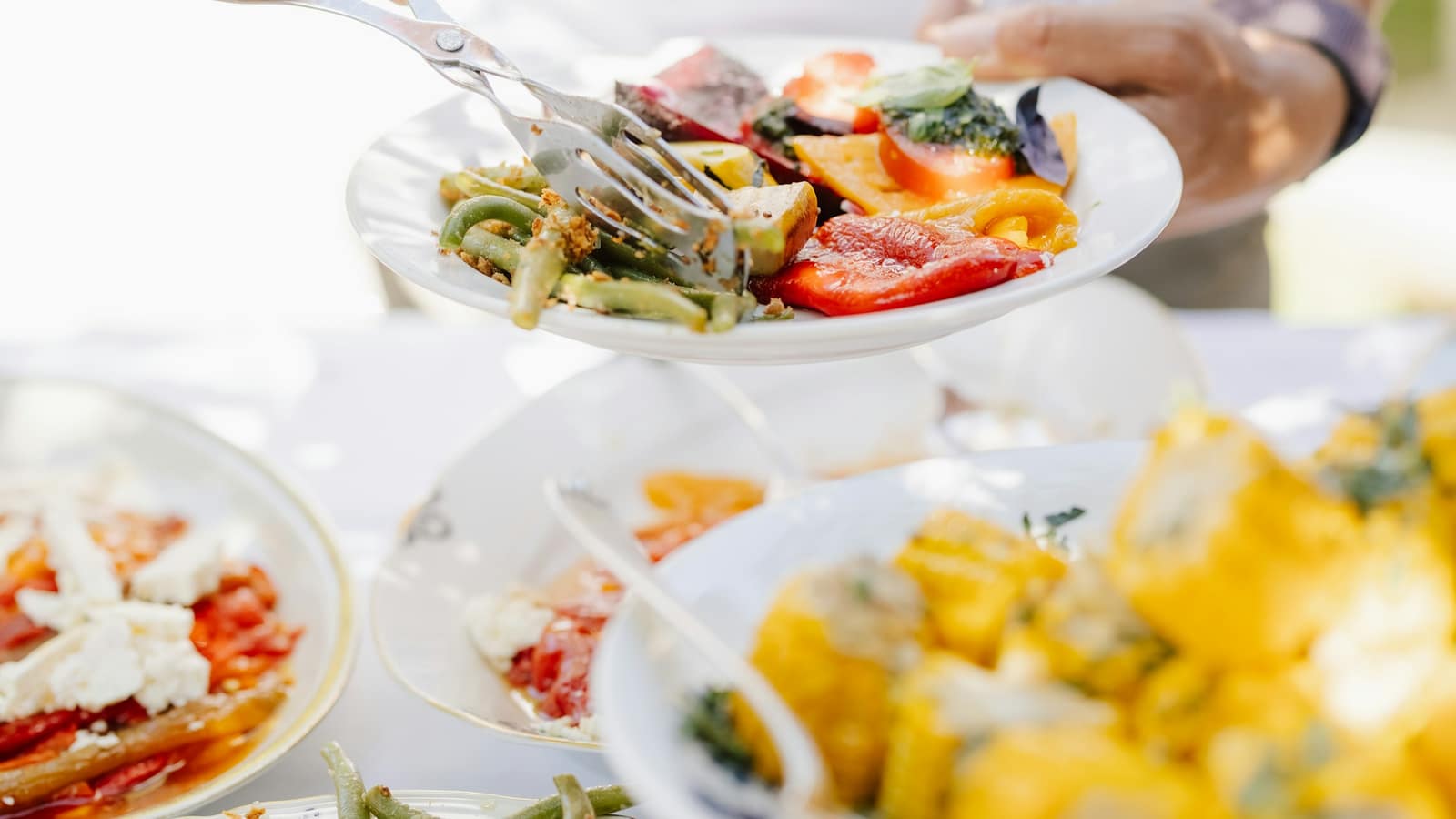 Prato de legumes grelhados sendo servido numa mesa ao ar livre, com travessas de salada ao lado