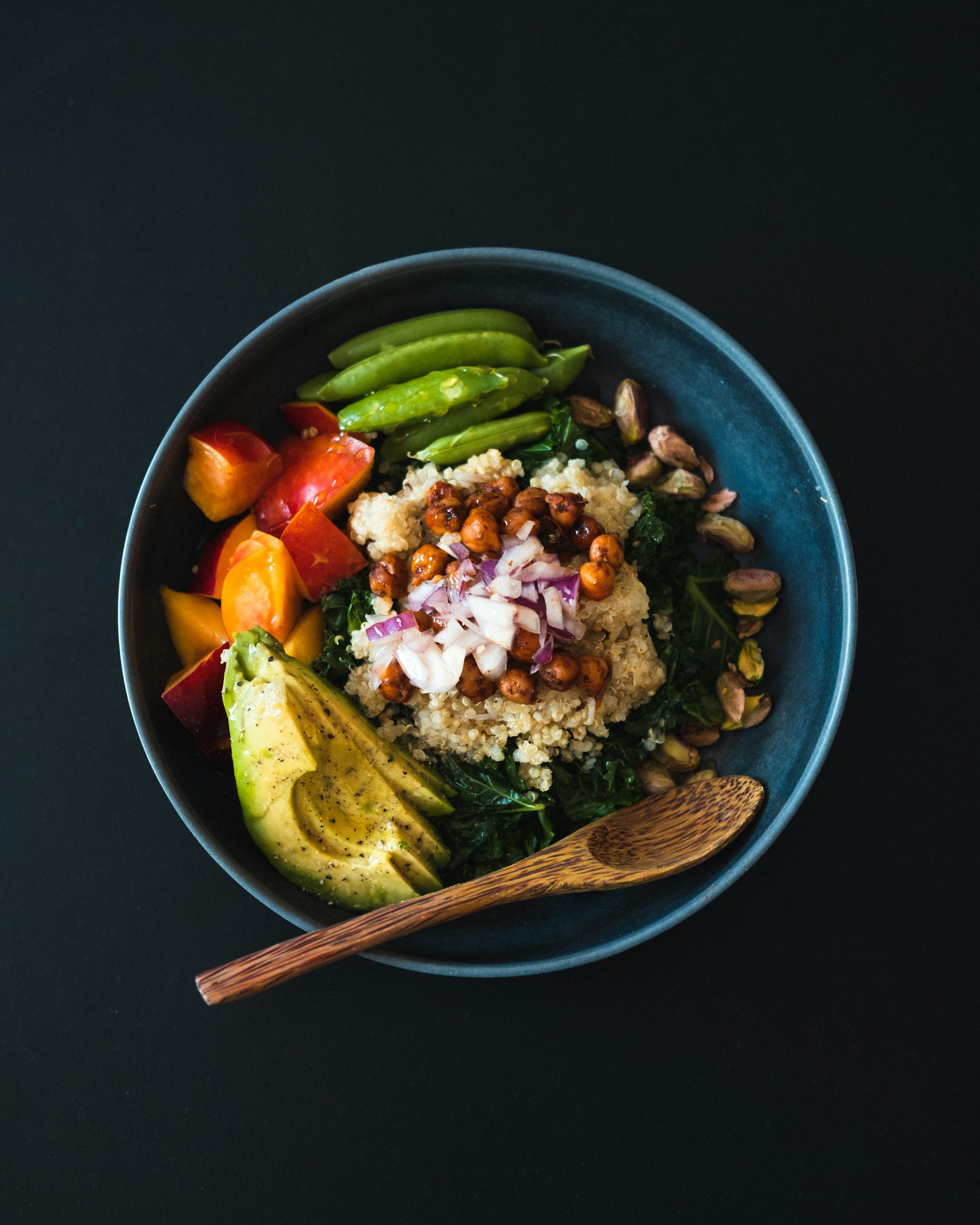 Bowl de quinoa, grão-de-bico, abacate e folhas verdes, visto de cima sobre fundo escuro