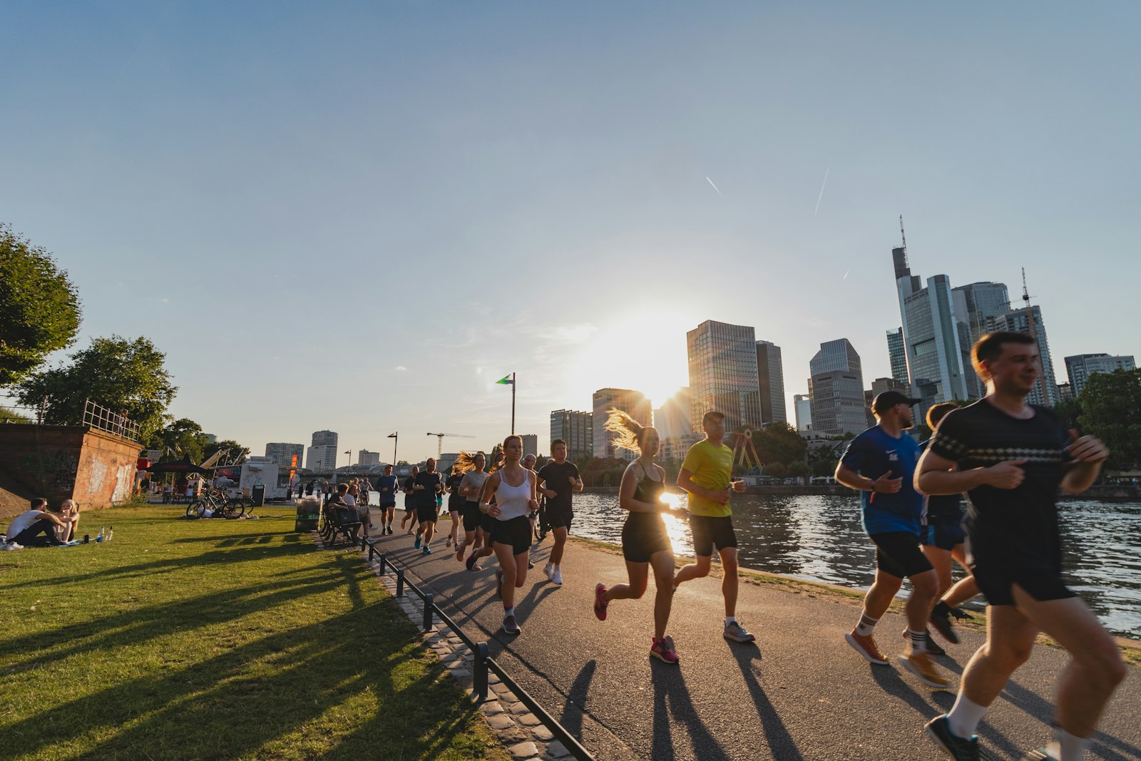 Grupo de corredores lado a lado em uma orla urbana no fim da tarde, prédios da cidade ao fundo
