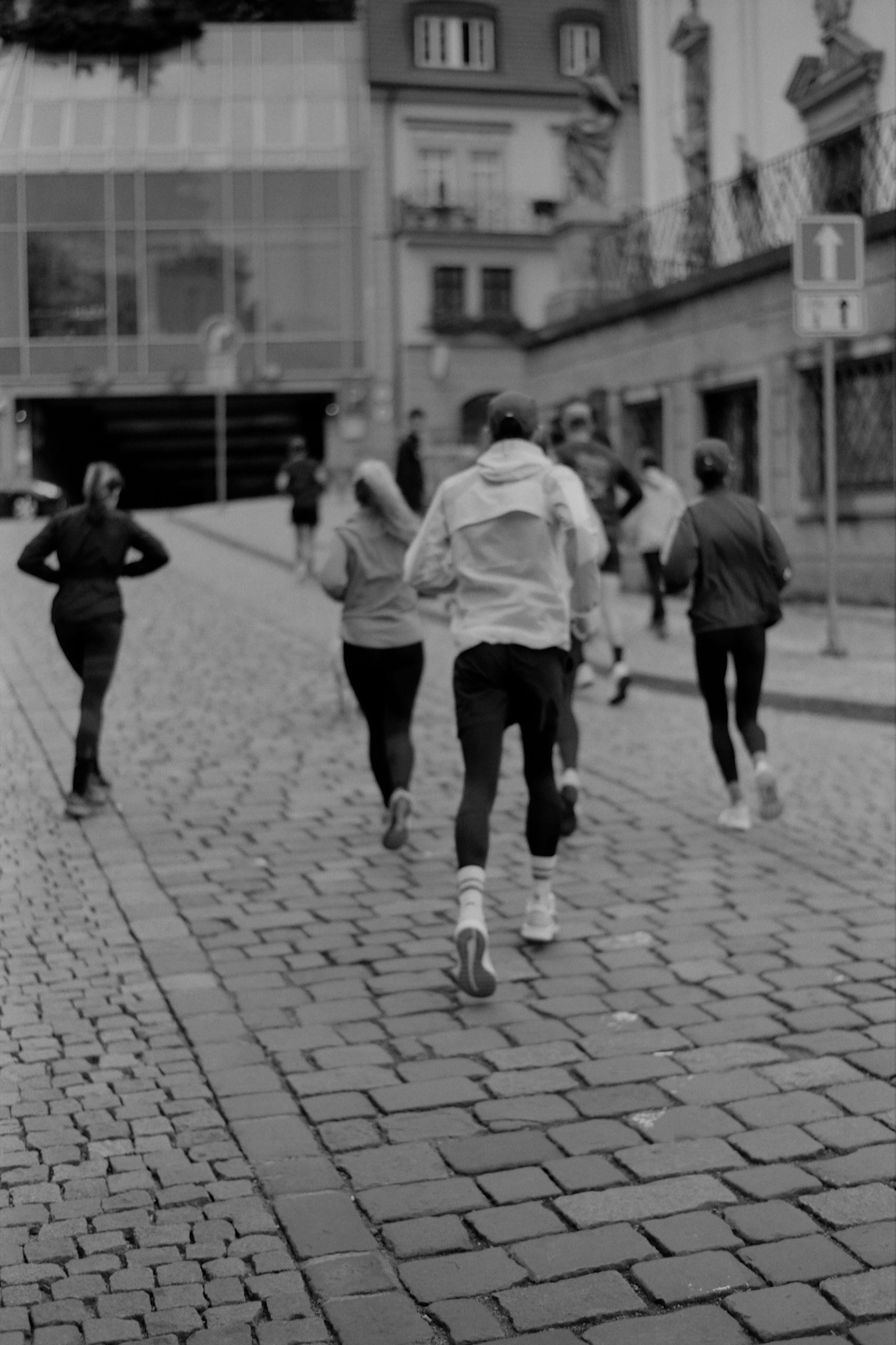 Grupo correndo junto por uma rua de pedras de centro histórico, de corta-vento e tênis de corrida