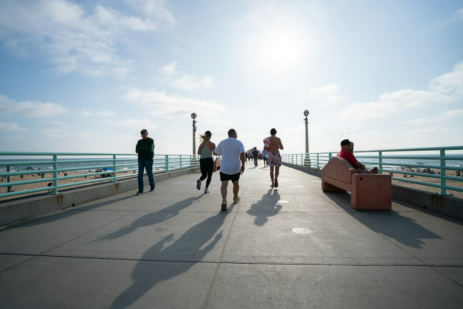 Pessoas caminhando e correndo em um calçadão à beira-mar sob o sol