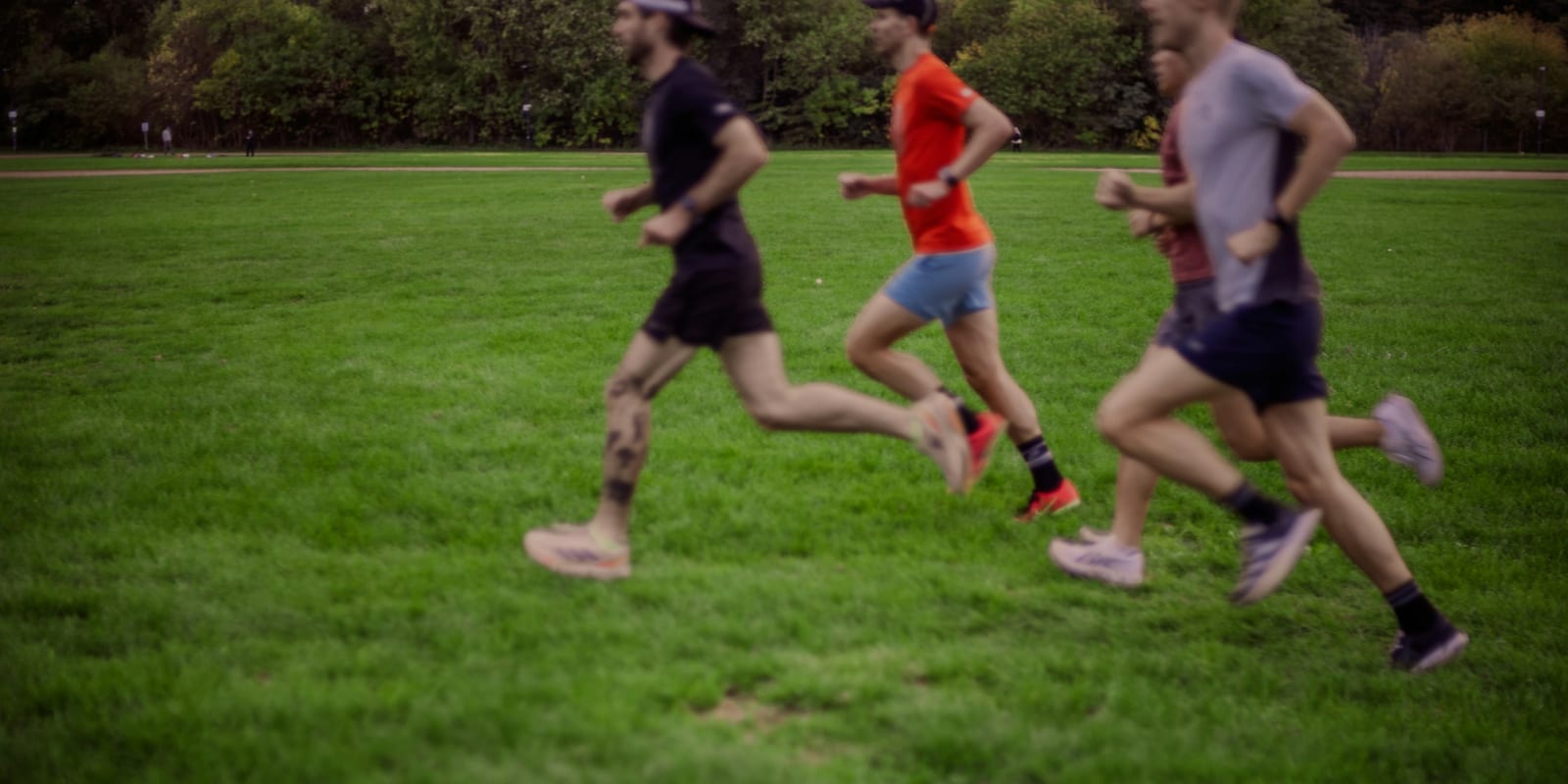 Três corredores em treino de grupo num gramado, em movimento